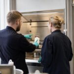 To medarbejdere ved et udsugningsskab under instruktion i kemikaliehåndtering